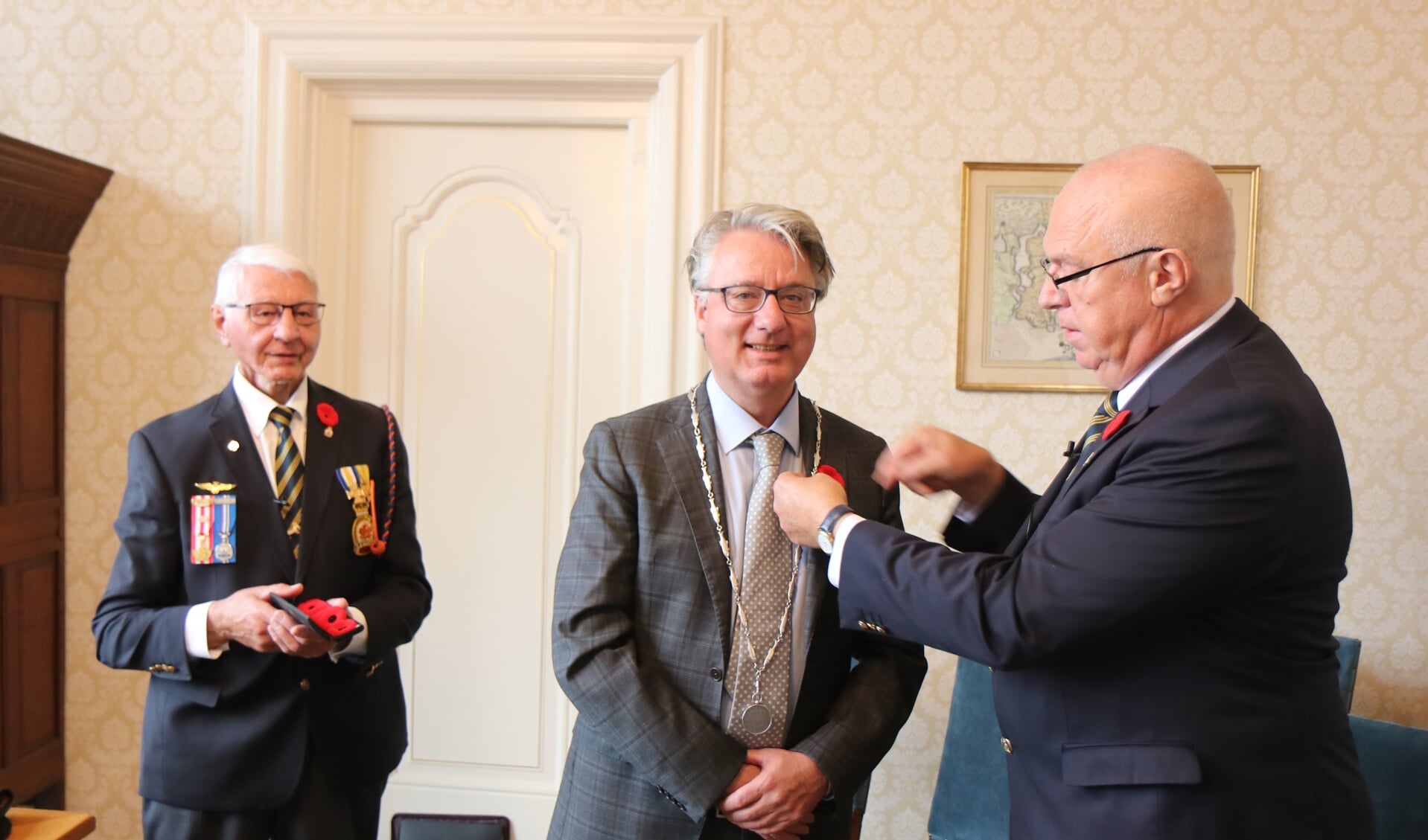 Ruud Janssen van The Royal Canadian Legion Branch 005 reikt de eerste Poppy uit aan burgemeester Moolenburgh. Veteraan Herman Sligman kijkt toe.