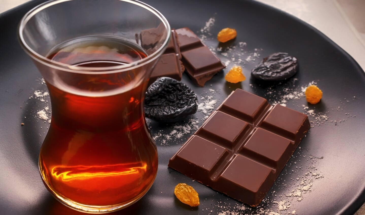 Chocolate, prunes, raisins and tea in a glass on a black plate. Soft light