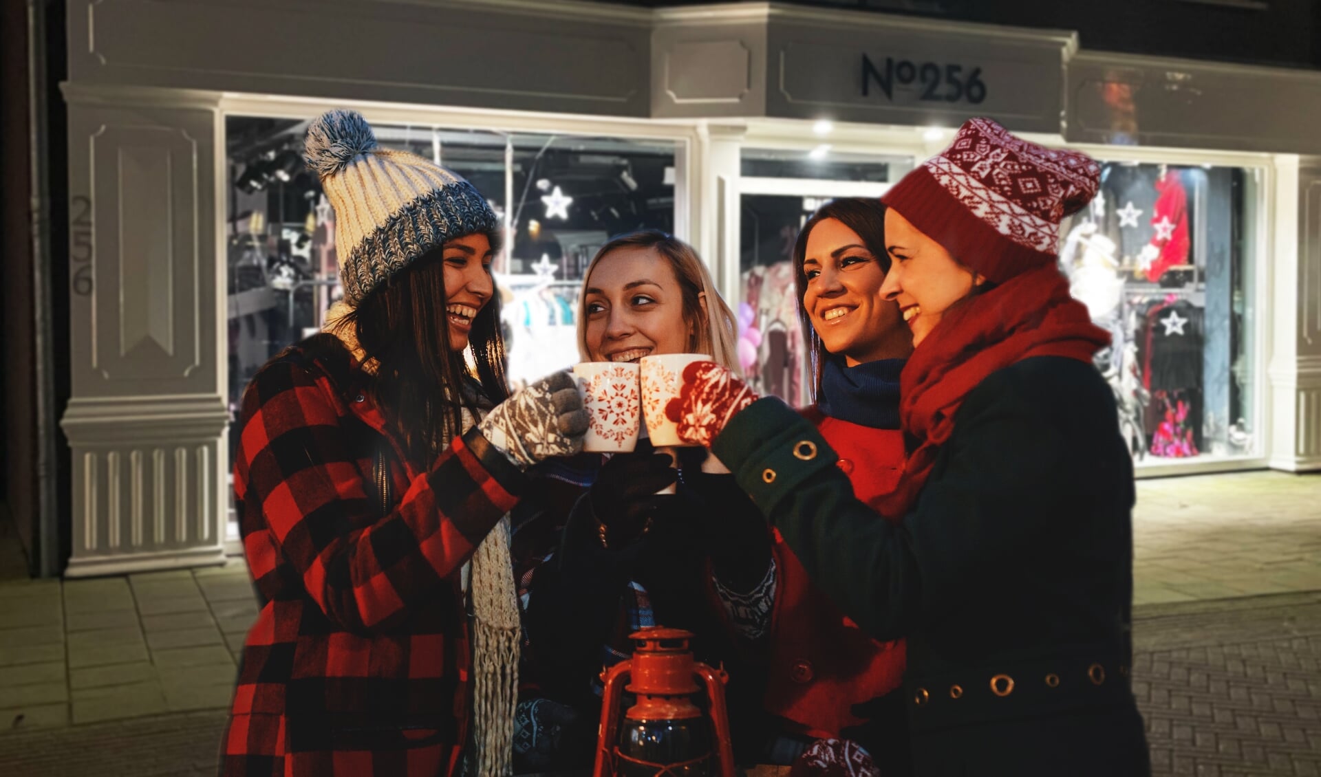 Group of friends enjoying the magic of Christmas by cheering with mulled wine and hot tea on a street at a city decorated with Christmas lights.