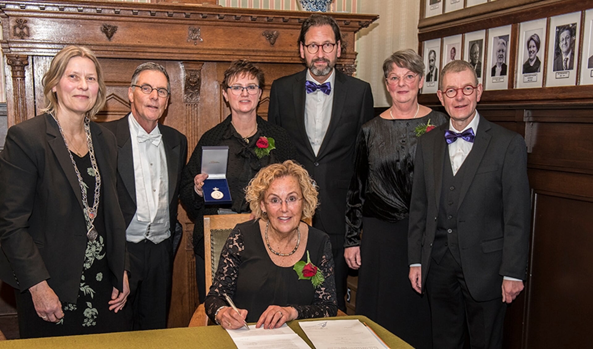 Voorzitter Addie Verspui tekent de papieren die horen bij de Koninklijke onderscheiding in het bijzijn van wethouder Molengraaf, dirigent en bestuur. 