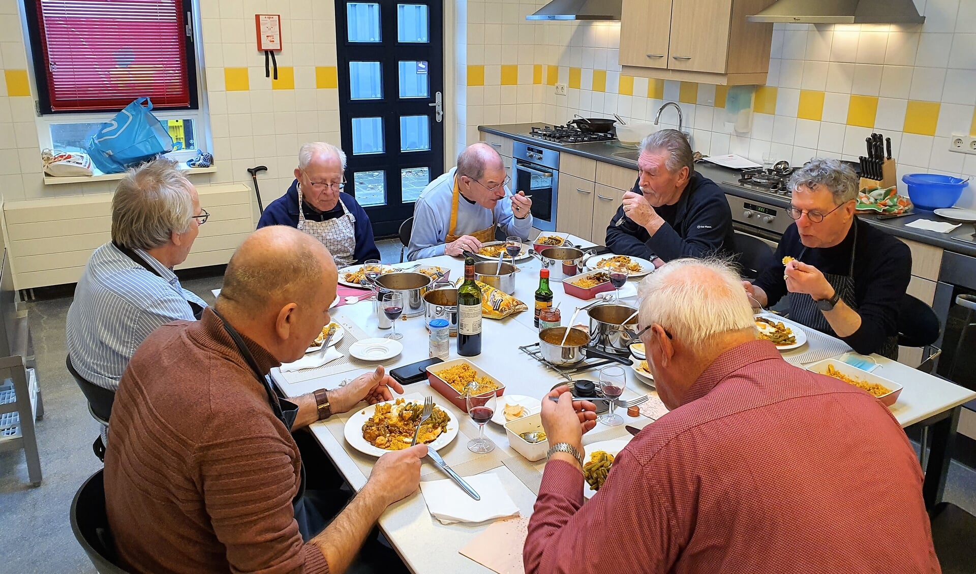 Smakelijk wordt door de kookcursisten de zelf bereidde maaltijd genuttigd. Op de voorgrond cursusleider Leo van den Berg.