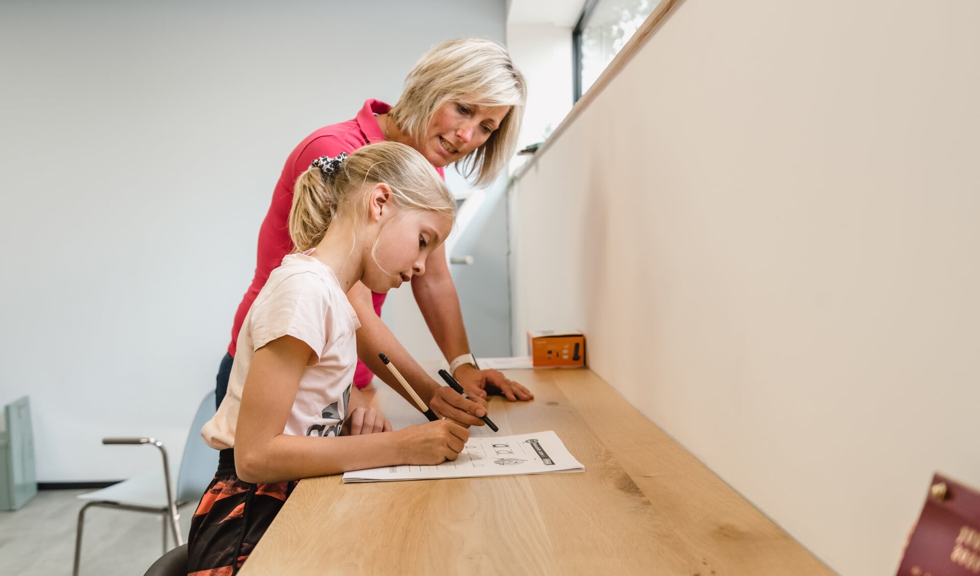 Kinderoefentherapeut Domini Meijer leert een kind schrijfvaardigheden.