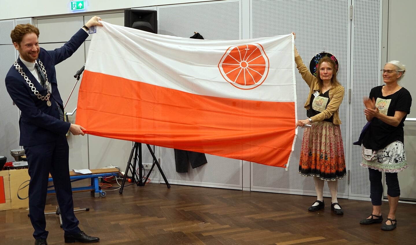 Burgemeester Floor Vermeulen en Paulette Klei (jubileumcommissie) tonen de vlag van Wageningen, het cadeau van de gemeente aan de Wieledansers