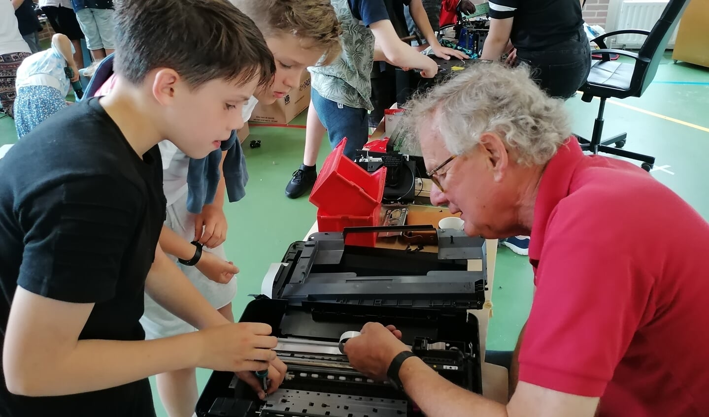 Oud en jong aan de slag bij het demonteren van een printer tijdens de techniekweek van basisschool De Bron.