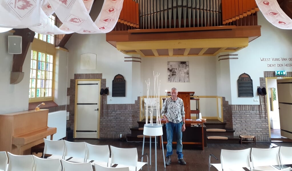 Roel Berg met zijn werk dat hoog in de kerk prijkt: ,,Kerk en kunst versterken elkaar
