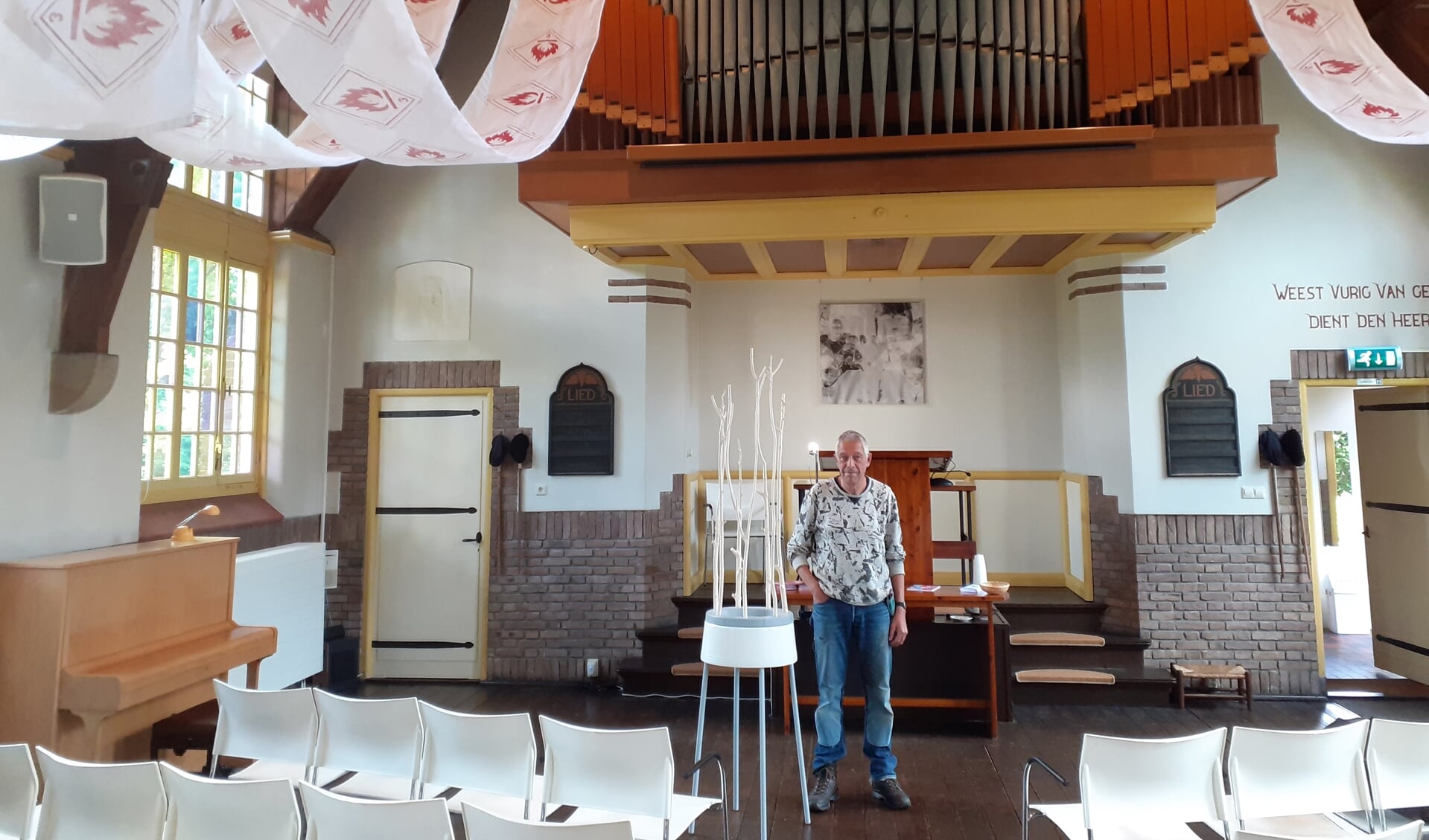 Roel Berg met zijn werk dat hoog in de kerk prijkt: ,,Kerk en kunst versterken elkaar