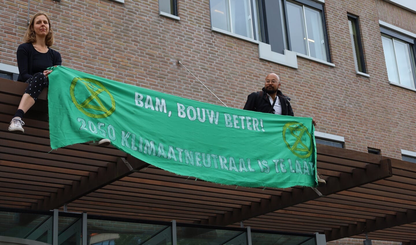 Twee christelijke klimaatactivisten houden een banner vast met de slogan: BAM, bouw beter! 2050 Klimaatneutraal is te laat.