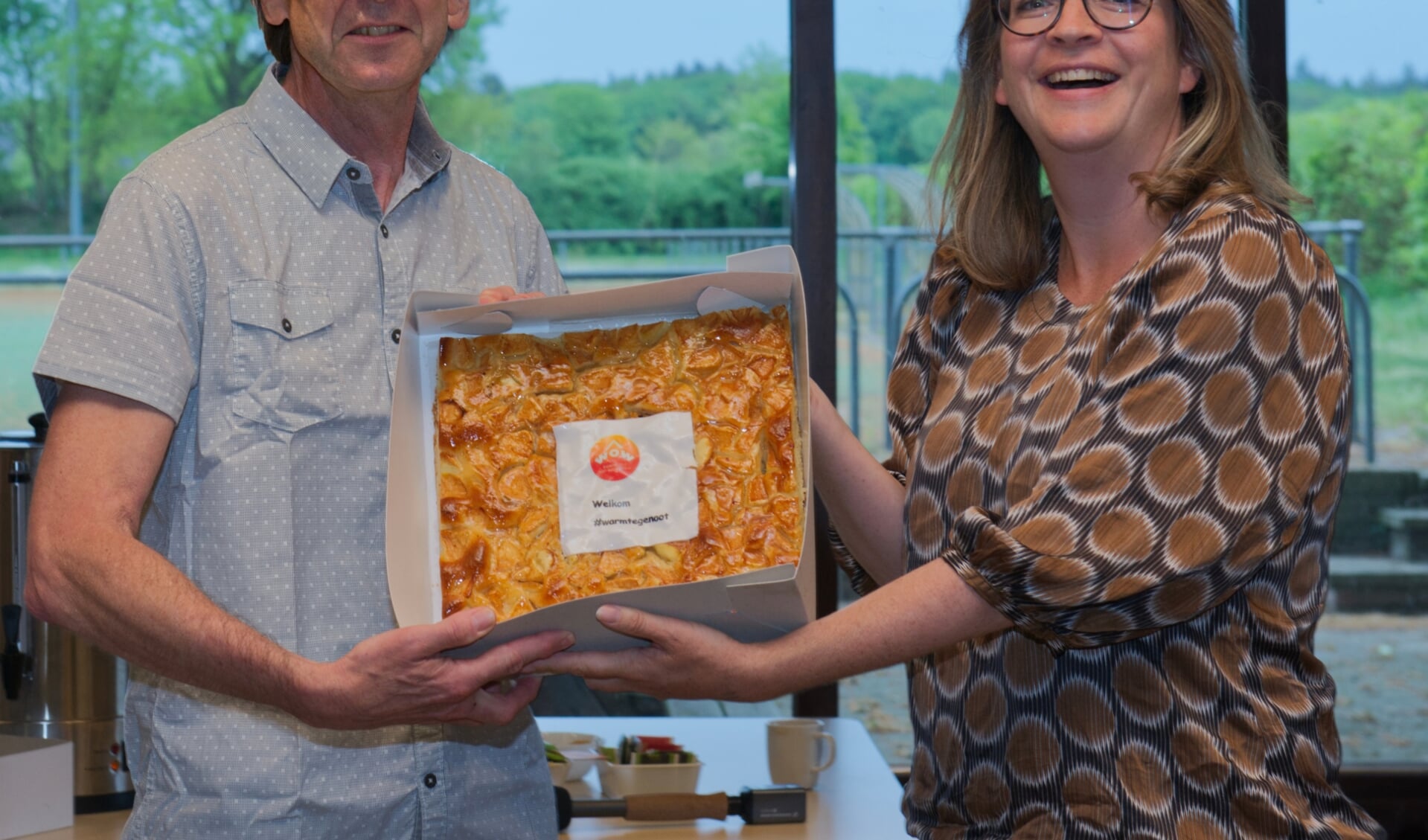 Wethouder Anne Janssen overhandigt een taart aan eerste WOW-klant Paul Goedhart
