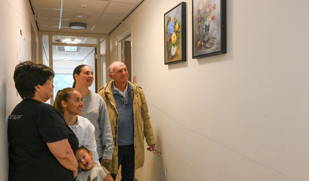 Peter Luitze (rechts) bekijkt met enkele Oekraïense vluchtelingen wat schilderijen die zijn opgehangen.
