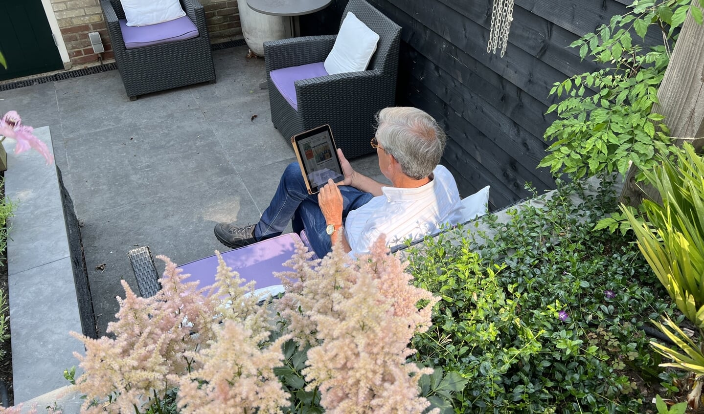 Pieter Schut leest de krant op zijn tablet in de tuin. 