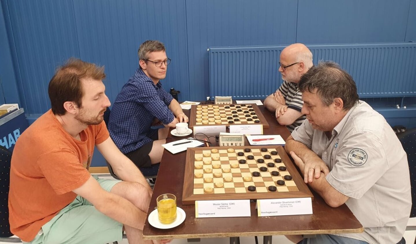 Toernooiwinnaar Alexander Schwarzman (rechts voor) denkt na over de beste zet tegen collega-grootmeester Wouter Sipma. Wereldkampioen Roel Boomstra (links achter) kijkt belangstellend toe. 