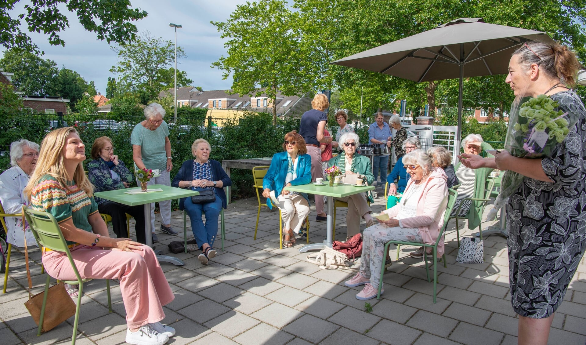 Katinka Verdonk (r) verwelkomt de ouderen op het zonnige terras bij Plein Geel met koffie en gebak.