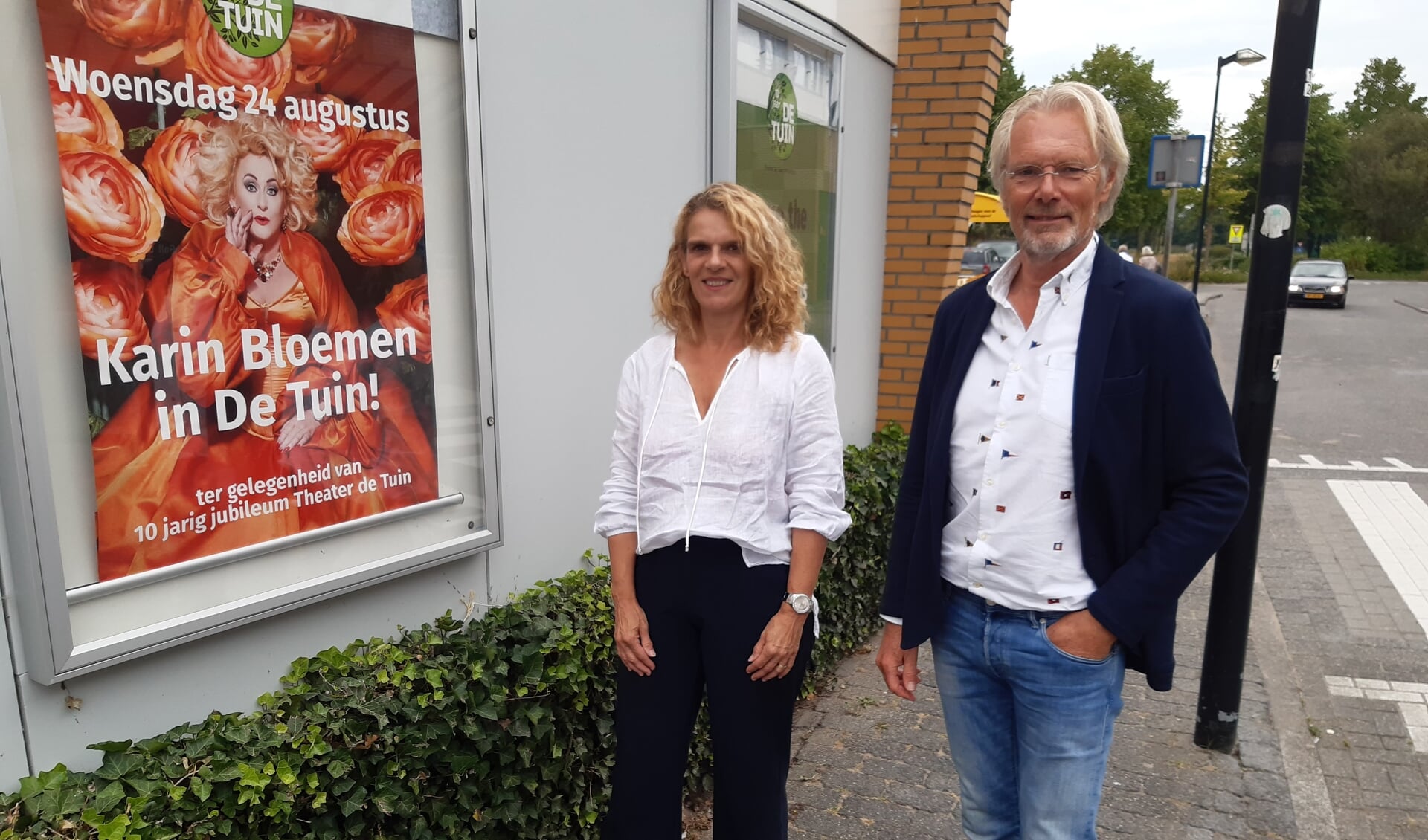 Programmaleider Jessica Kroeske en voorzitter Wim Oeben poseren bij de poster van de jubileumvoorstelling van Karin Bloemen.