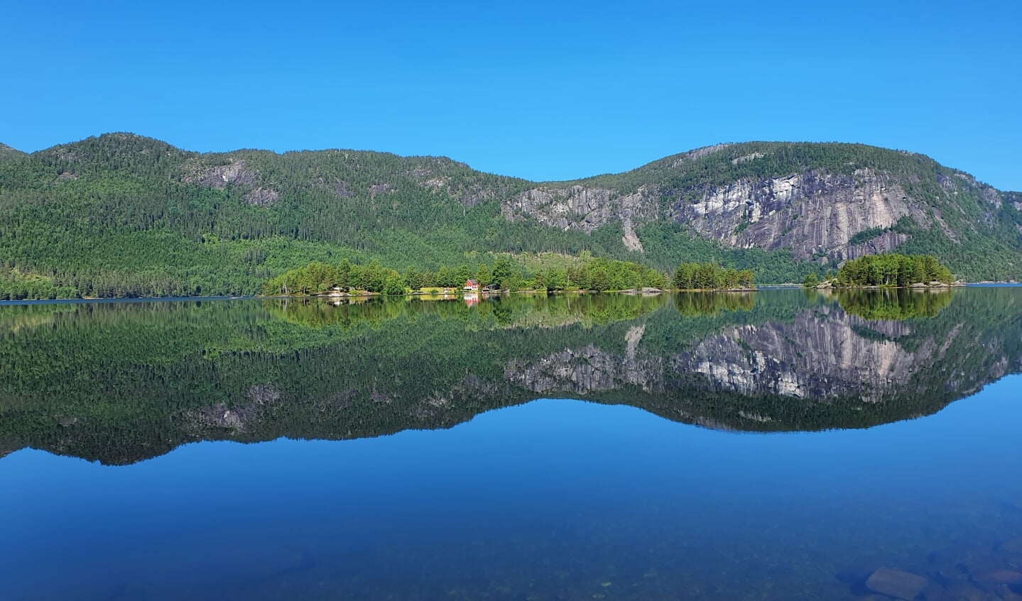Deze foto is gemaakt tijdens onze rondreis in Noorwegen. Hij is gemaakt op 30 juni 2022 in Bygland, met een prachtige blauwe lucht en een spiegelvlak meer.