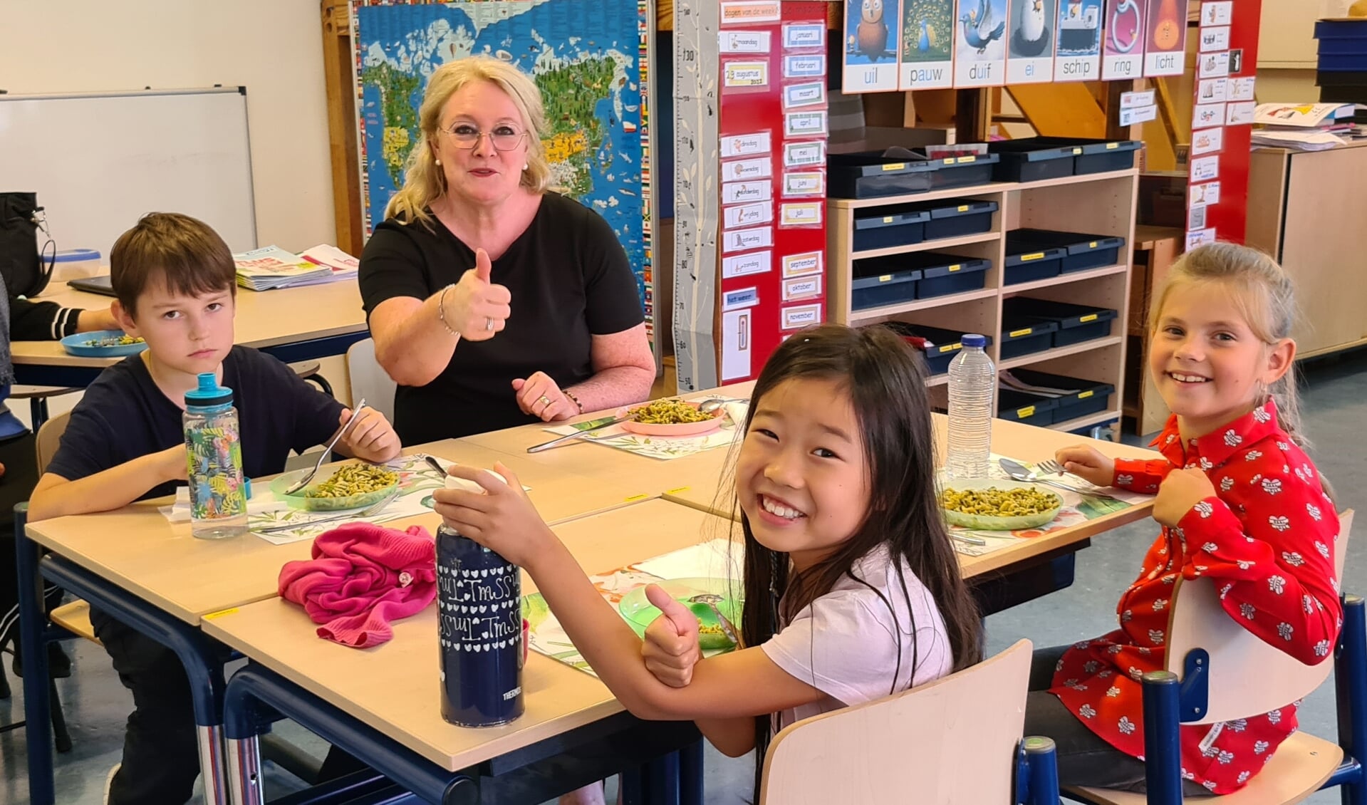 Leerlingen van OBS De Wereld genieten met de schooldirecteur en de overblijfjuf van de eerste warme lunch: volkorenpasta met spinazie en tomaatjes.