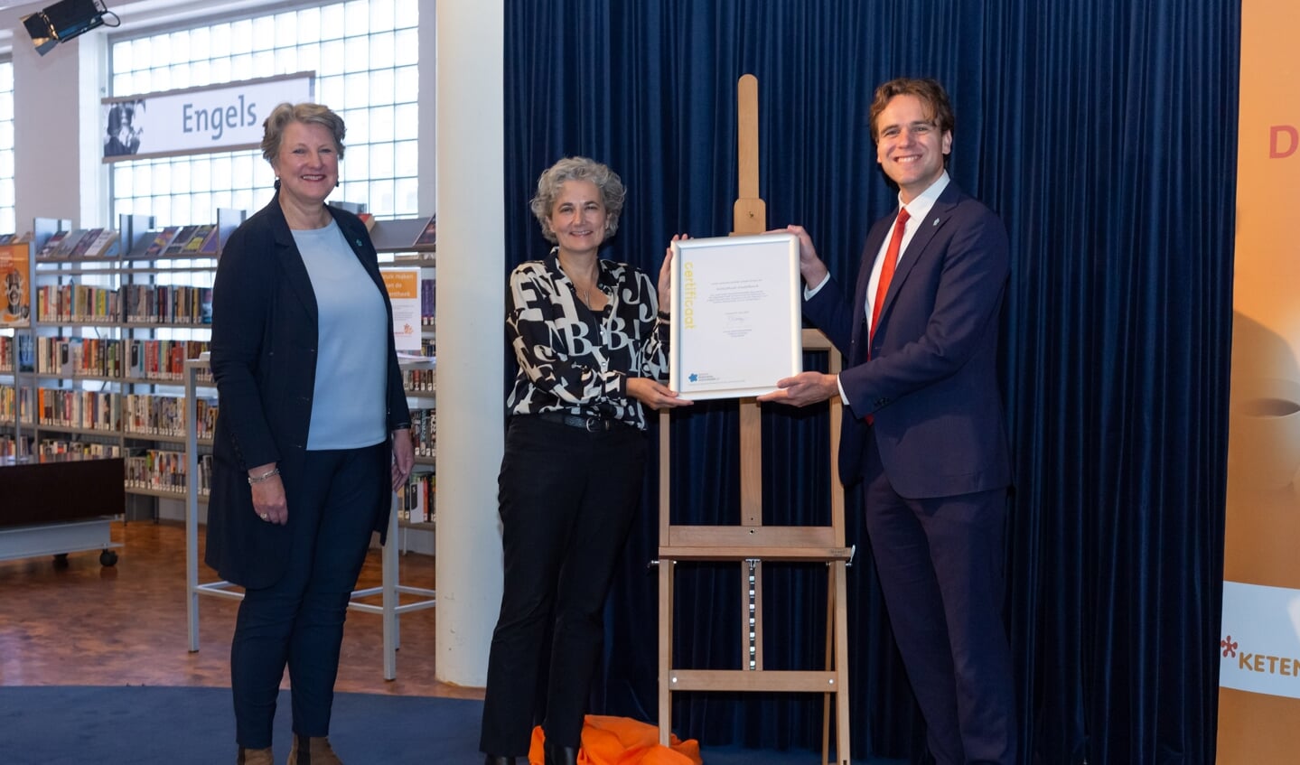 Marijn van Ballegooijen overhandigt het certificaat
dementievriendelijke bibliotheek aan bibliotheekdirecteur Daphne Janson. Links: Marga van Beek van Alzheimer Amstelland.
