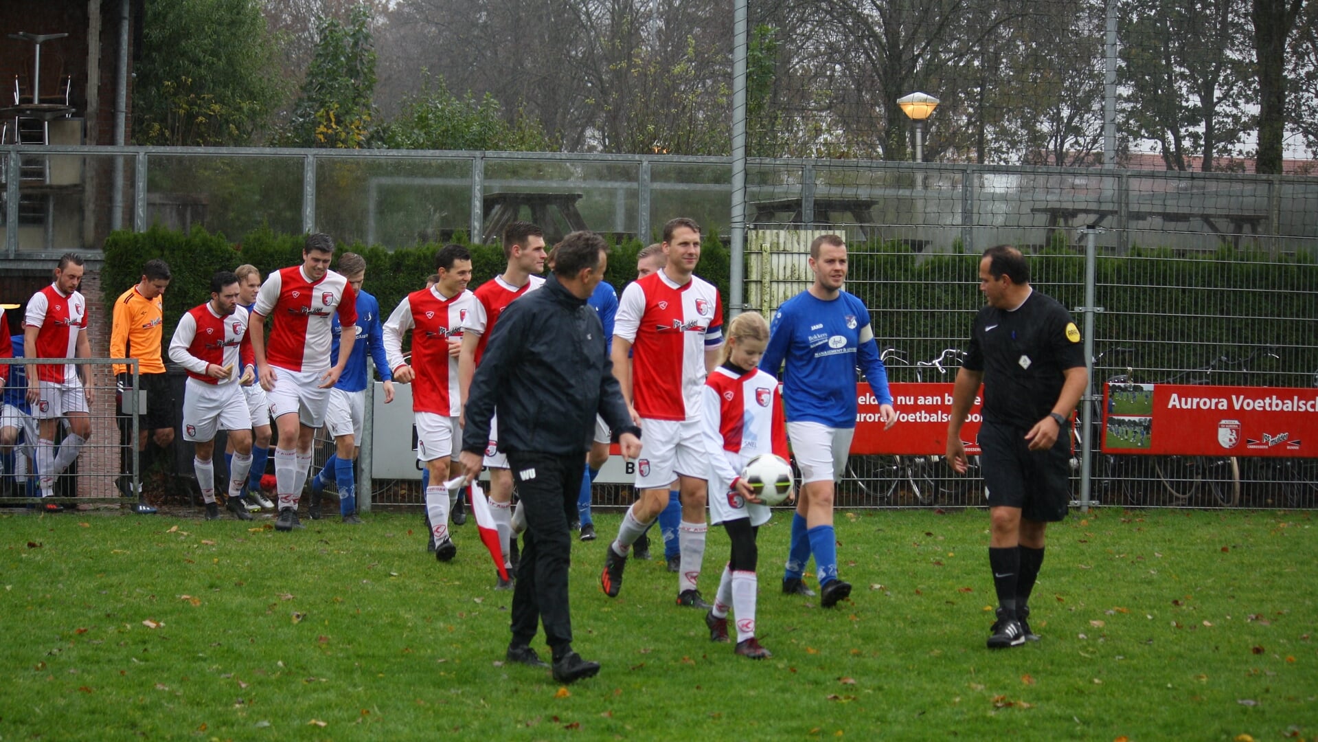 Opkomst van beide ploegen met in het midden Pupil van de Week Ine Verkerk.