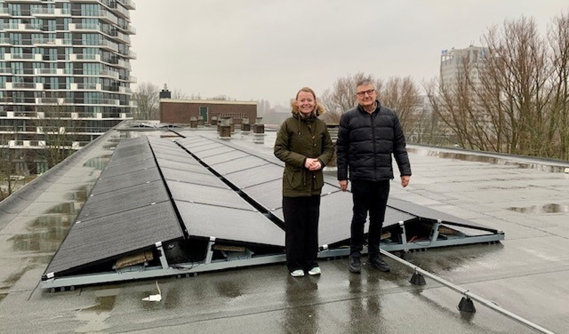 Wethouder Floor Gordon met Wouter Simonis (bestuurslid VvE Biesbosch) bij de zonnepanelen op het dak van het appartementencomplex.