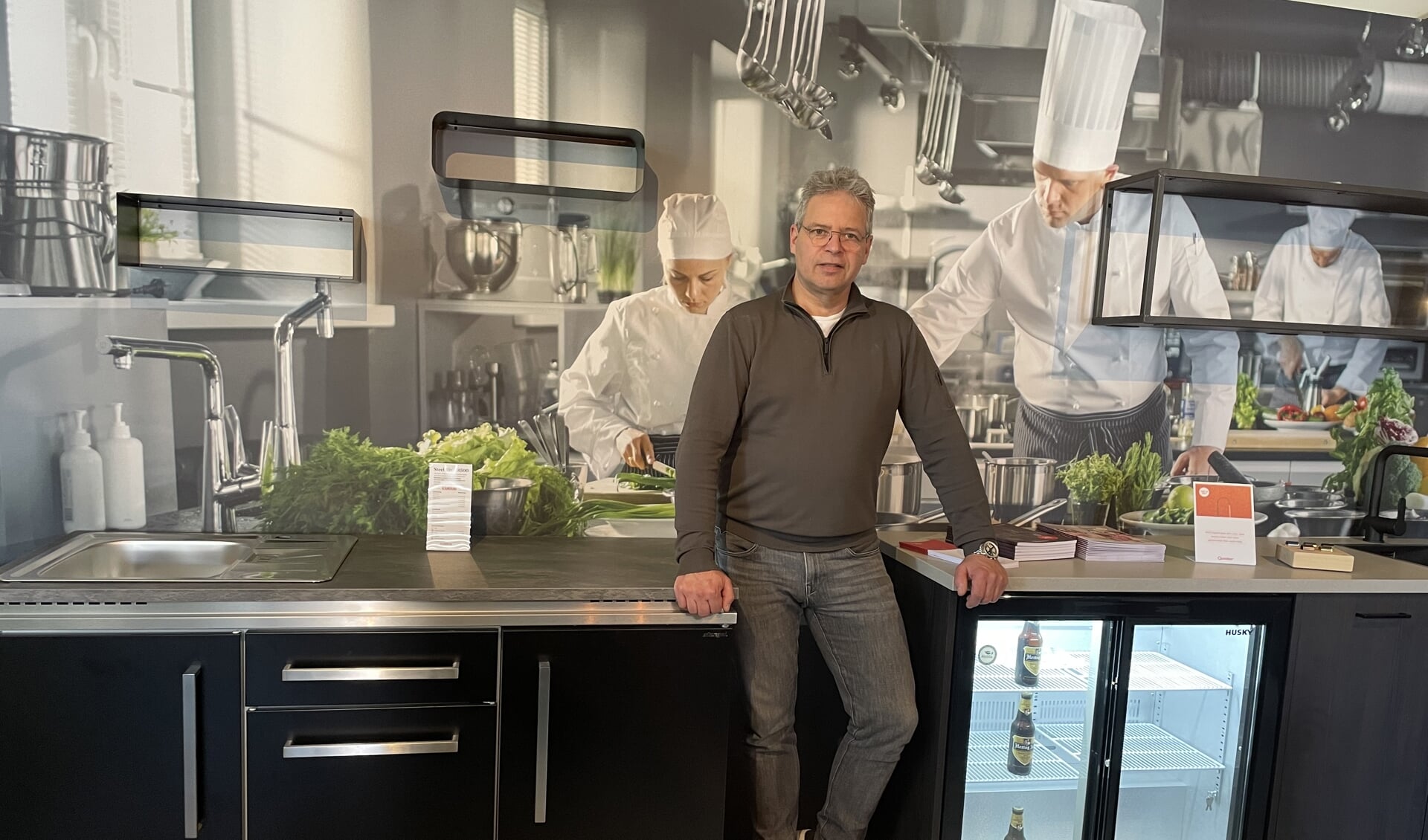 Gert Huisman in de showroom met een 'steel-lijn' keuken en een standaard keuken met glasdeurkoeling.