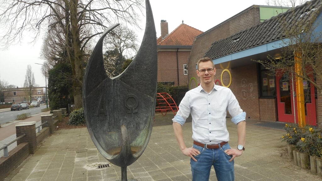 Schoolleider Reinier Vink op het schoolplein bij het logo dat al 100 jaar het logo is van de Patrimoniumschool, een opengeslagen boek en een duif ineen.