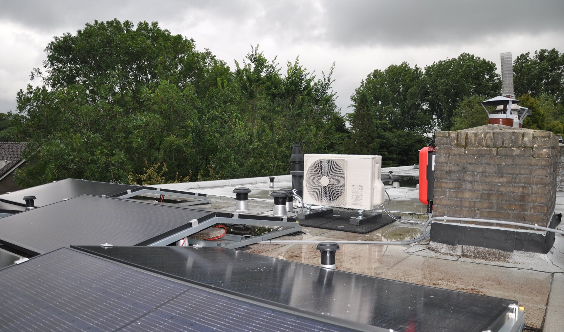 Buitenunit van hybride warmtepomp op een plat dak, waarop in dit voorbeeld ook zonnepanelen liggen.