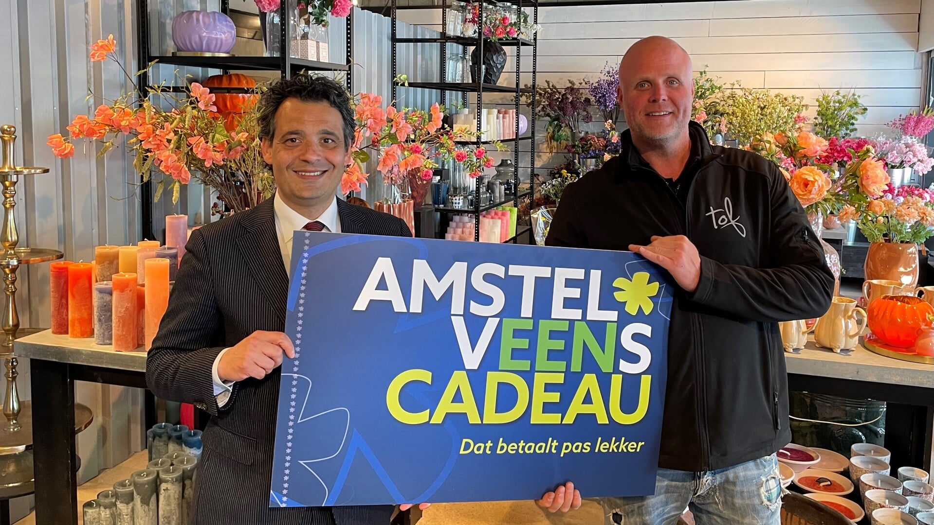 wethouder Adam Elzakalai feliciteert Henk Anrochte van TOF Bloemen omdat zijn zaak zich als 100ste bedrijf bij Amstelveens Cadeau heeft aangesloten