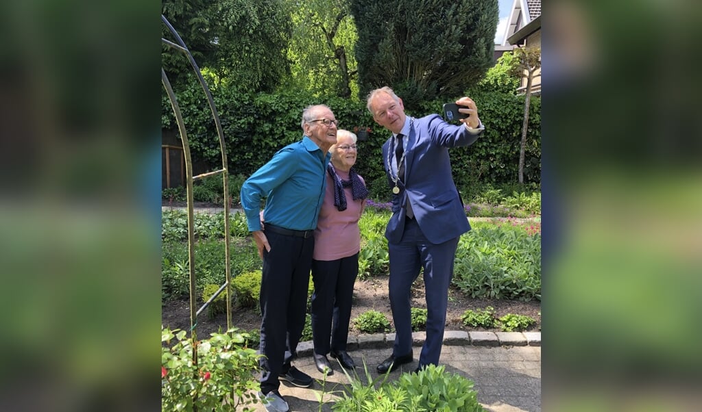 Jos en Greet van Benthem poseren voor een selfie met burgemeester Röell in hun bloemrijke tuin.