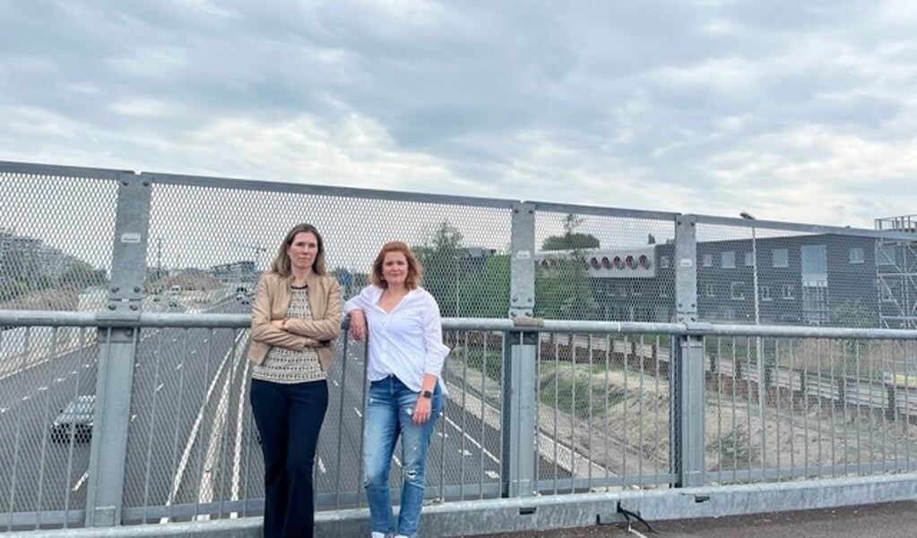De VVD-raadsleden Femke Lagerveld en Elisa De Marco (rechts) op de tijdelijke brug boven de A9. Aan weerskanten van de snelweg staan schoolgebouwen.