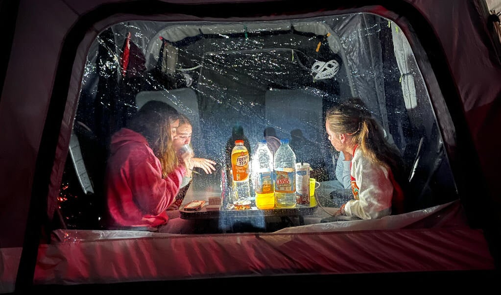 Deze foto is gemaakt op 3 augustus in Lacanau Frankrijk.
Tijdens een regenachtig dag op de camping hebben we een gezellige spelletjesavond gehouden. De foto is gemaakt van buiten naar binnen en geeft een mooi inkijkje in de tent en op de geconcentreerde gezichten. Omdat de lamp achter de flessen drinken staat word je er niet door verblind, maar wordt alles om de lamp heen mooi verlicht, net zoals de regendruppels op het plastic raam. De foto krijgt er bijna een Rembrandtsfeertje door. Het weerspiegelt een mooie tijdsgeest: kamperen, Oasis, Icebtea, een kabel om de telefoon mee op te laden en een fietshelm op de achtergrond. Maar welk spel zitten ze nu te spelen? Voor mij een weet, voor de kijker een raadsel.