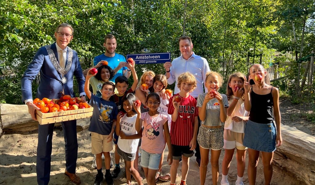 Burgemeester Poppens deelt fruit uit aan leerlingen van de Westwjizer. Achter hen JOGG-regisseur Sven Kuit  en JOGG-ambassadeur Patrick Rijnbeek (rechts) met het JOGG-plaatsnaambord. 