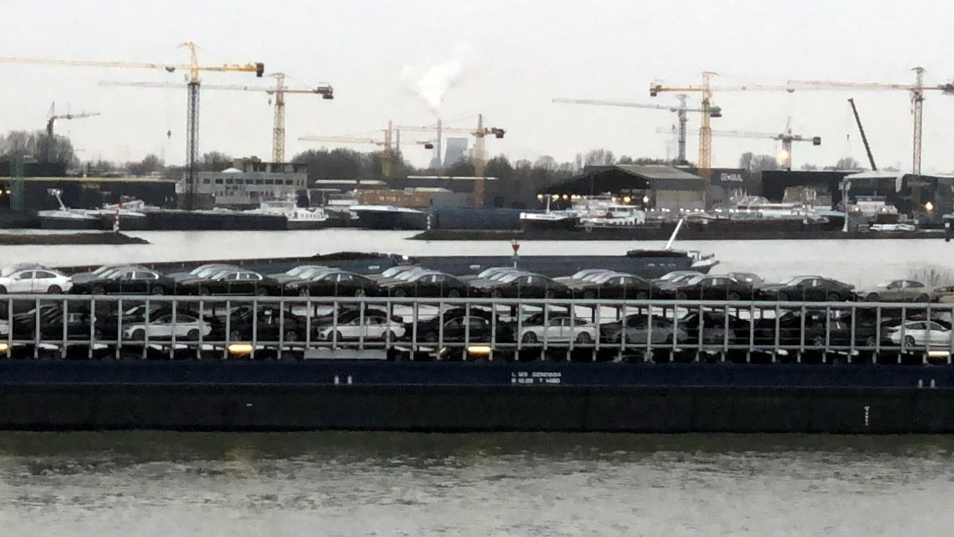 Een binnenvaartschip met auto's aan boord; op de achtergrond is de haven van Werkendam te zien