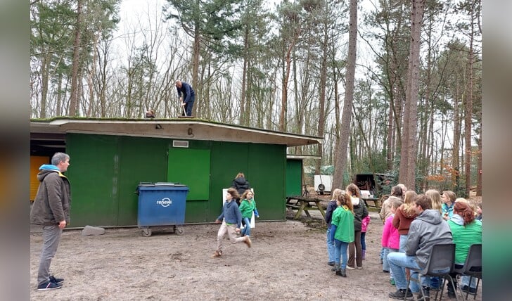 Terwijl jonge scouts zich vermaken, veegt een ouder het dak van het clubgebouw van De Fakkeldraagsters schoon.