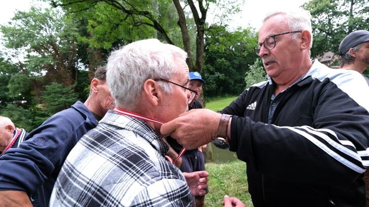 De Voorn-voorzitter Henk van Ingen hangt een van de deelnemers aan de Zideris-viswedstrijd een medaille om.