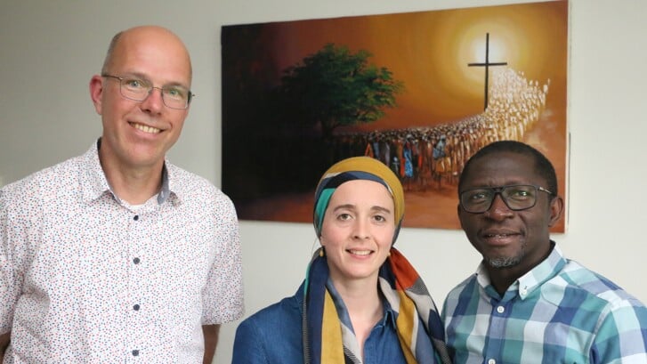 Vlnr: Jan van den Brink, Marinne en Lucky Simon, samen voor een schilderij uit Nigeria met een godsdienstige betekenis.