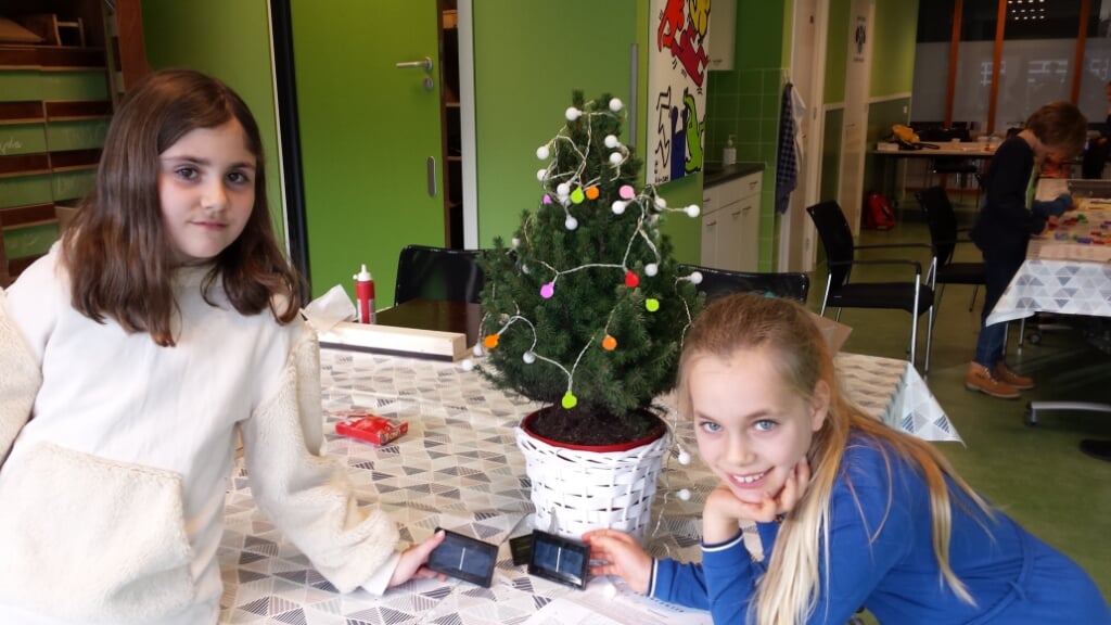 Plusklasleerlingen Lou en Elise tonen in het lokaal van Cultuurhuis Schoneveld het kerstboompje met verlichting op zonne-energie.