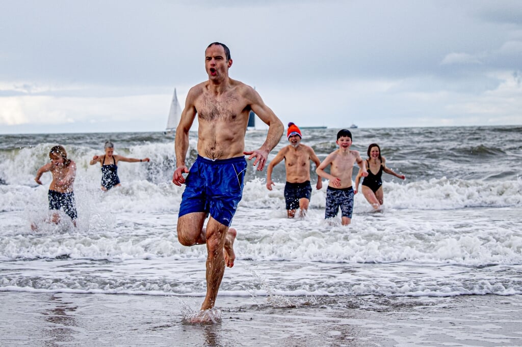 2021-01-01 11:53:14 SCHEVENINGEN - Mensen rennen de zee in bij het strand van Scheveningen op Nieuwjaarsdag. De traditionele Nieuwjaarsduik is vanwege de coronacrisis afgelast. ANP ROBIN UTRECHT