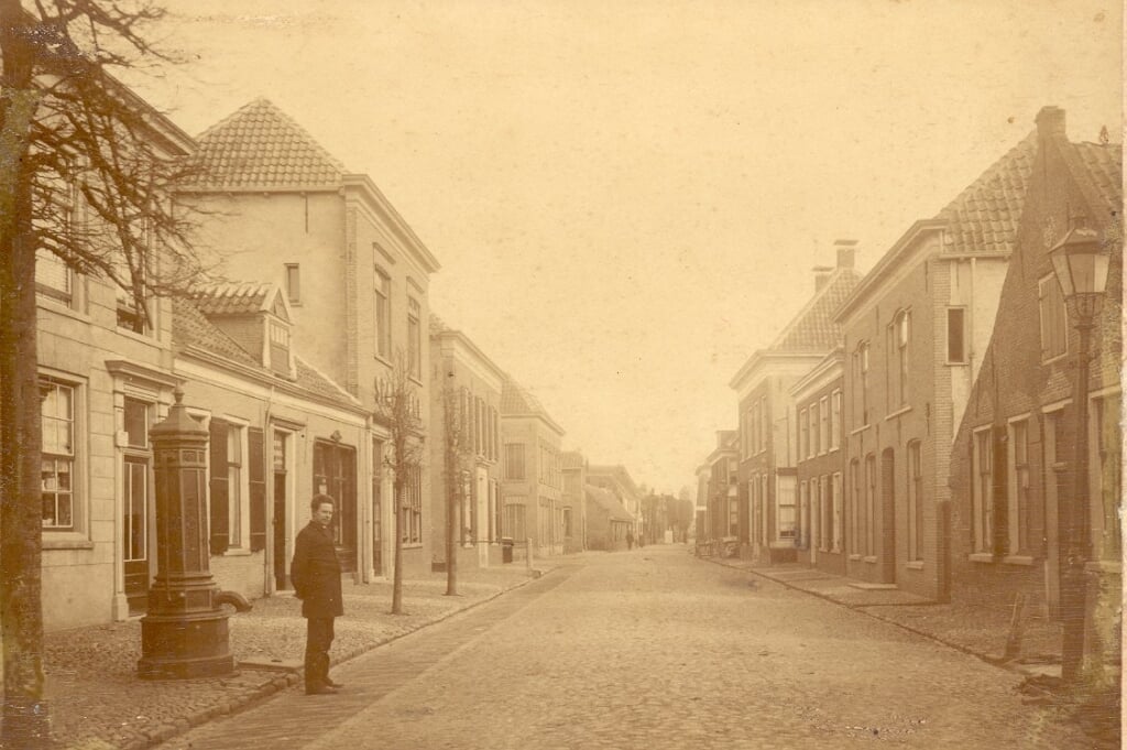 Een oude foto van dit gedeelte van de Langstraat, met links de bakkerij van Nicolaas Balt. Achter de naar de fotograaf kijkende man een gietijzeren pomp waar drinkwater kon worden gehaald.