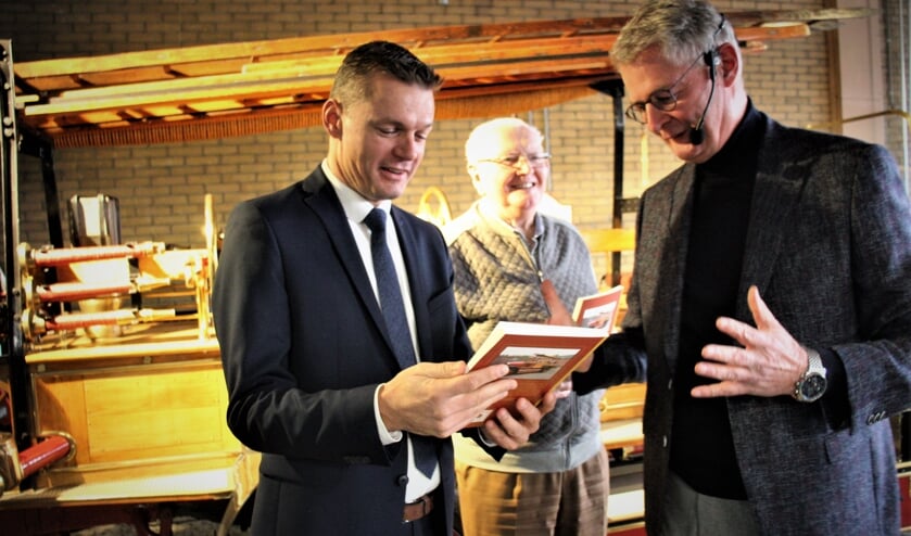 Burgemeester Nieuwenhuis krijgt uit handen van auteur Hans Zuidijk één van de twee eerste exemplaren. Toon van Nielen kijk toe.