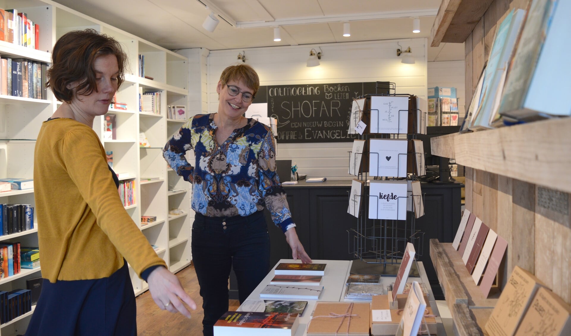 Mariëlla Koppenaal en Elly van Hoffen in de winkel met boeken, cadeautjes, kaarten en een koffiehoekje.
