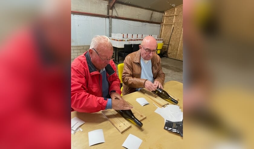 <p>Initiatiefnemer Cor van den Berg (rechts) en mede-Lion Cees Bloot etiketteren de flessen.</p>