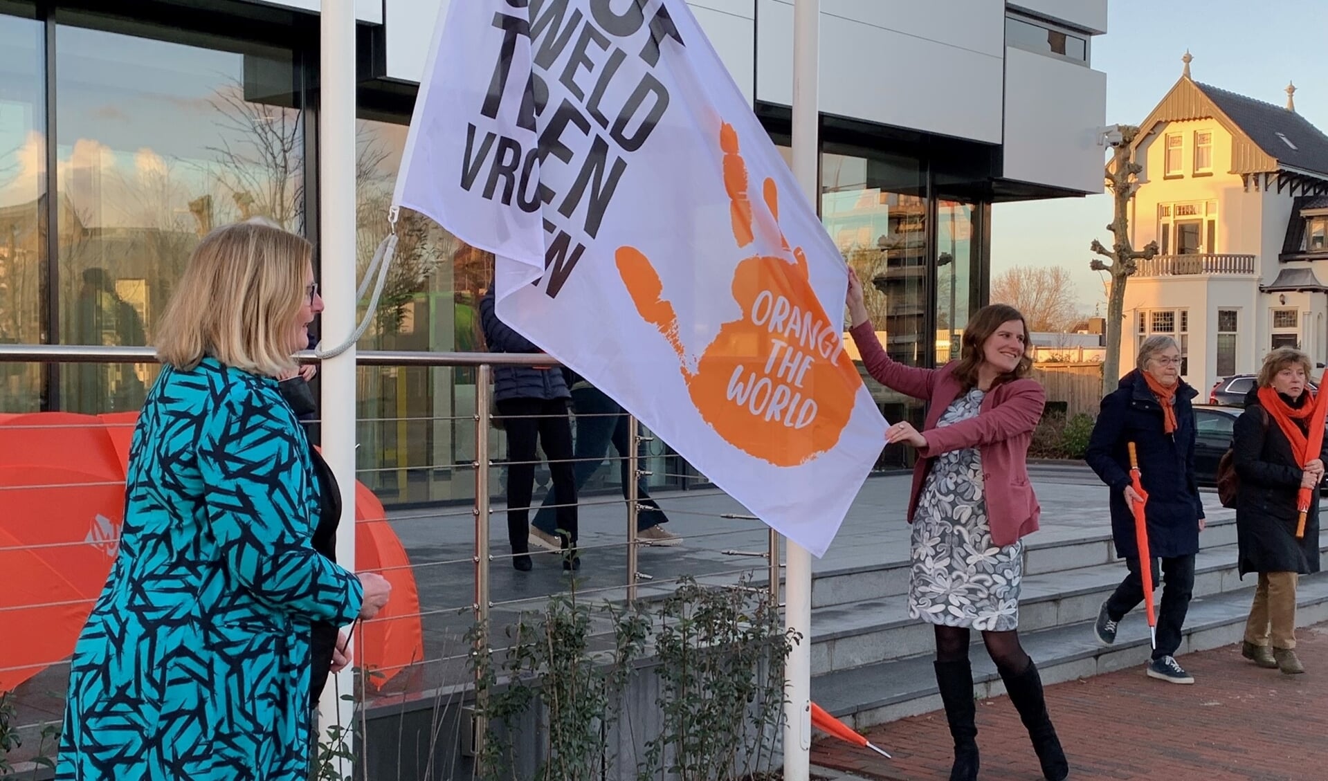 Wethouder Leferink (links) en wethouder Vleij hijsen bij het gemeentehuis in Waddinxveen de vlag voor Orange the World. (foto: pr)