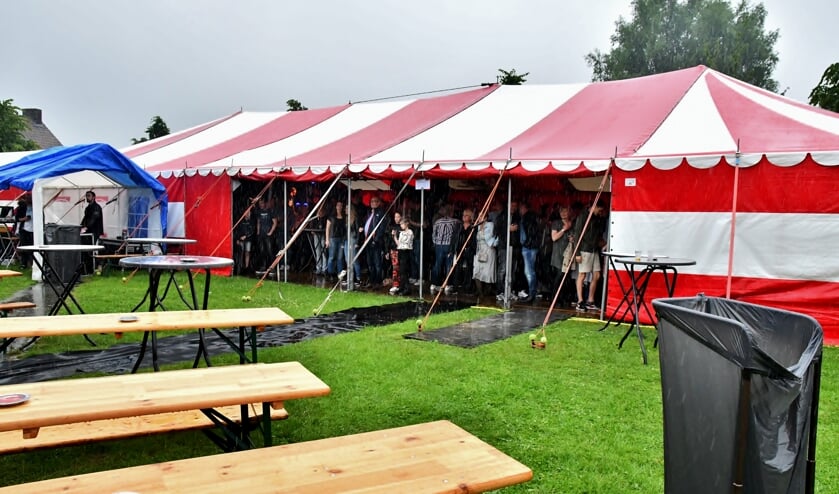 Bezoekers van Limuscene bekijken de acts in de kiosk van een afstandje, beschut tegen de regen in de feesttent.