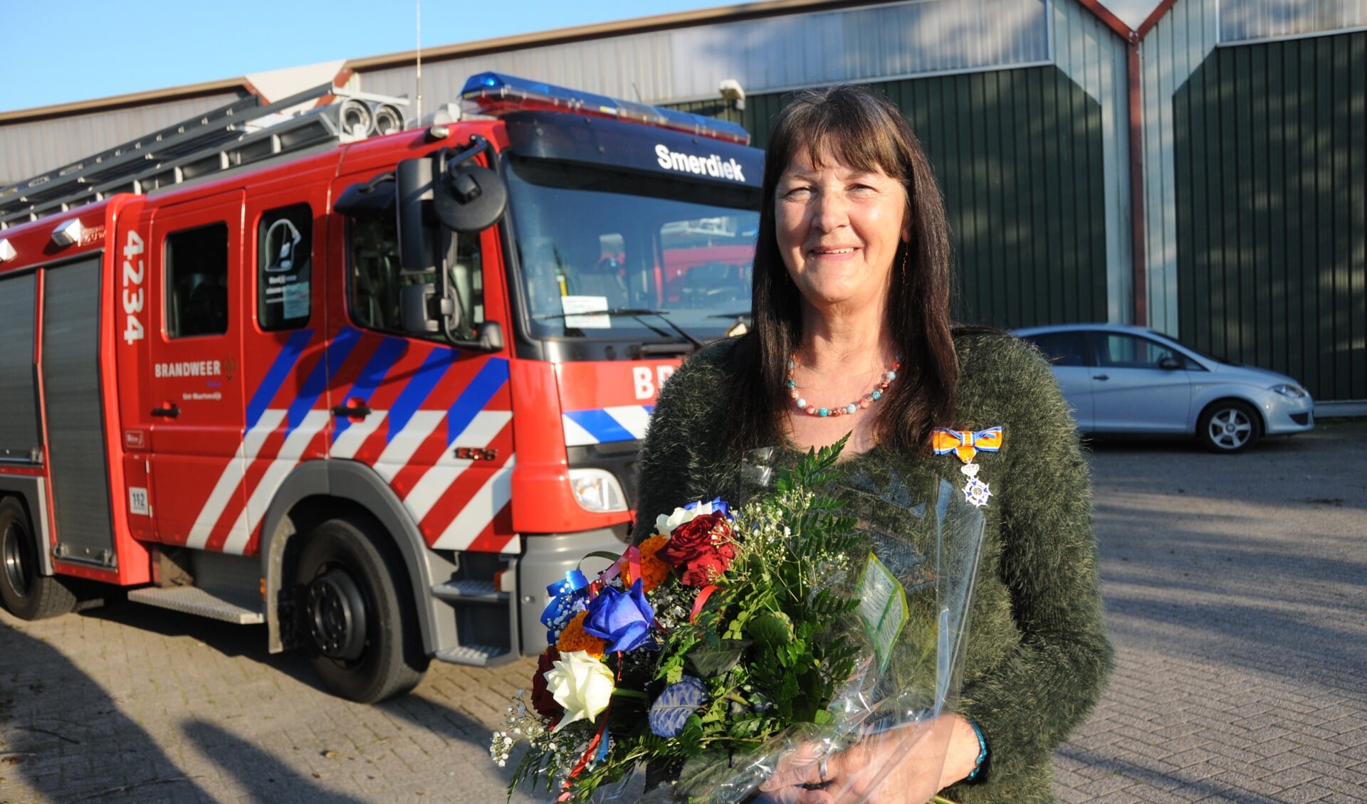 Addie Giljam met lintje en bloemen bij de brandweerwagen van Smerdiek.