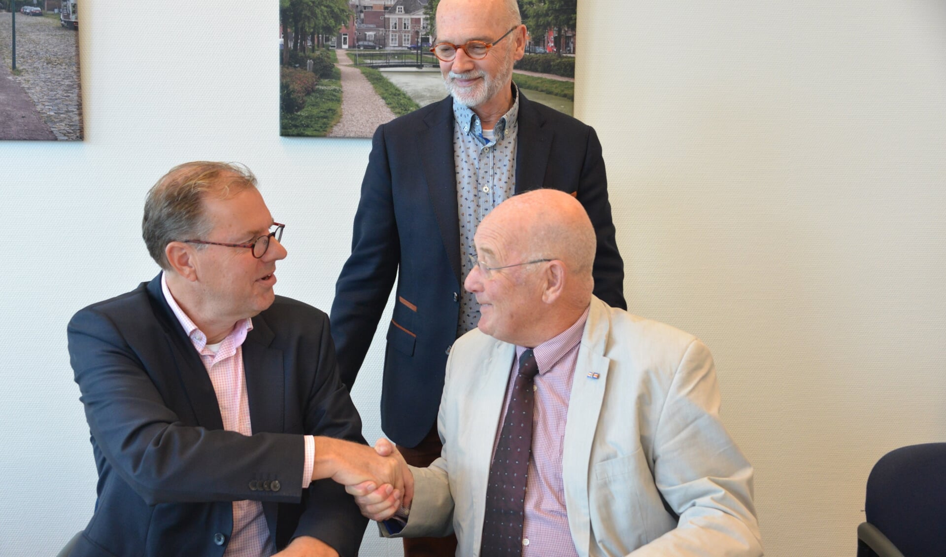Voorzitter Jan Legierse (rechts) en wethouder Koos Krook bezegelen de overeenkomst met een handdruk. Penniingmeester Rien van Zundert kijkt toe.