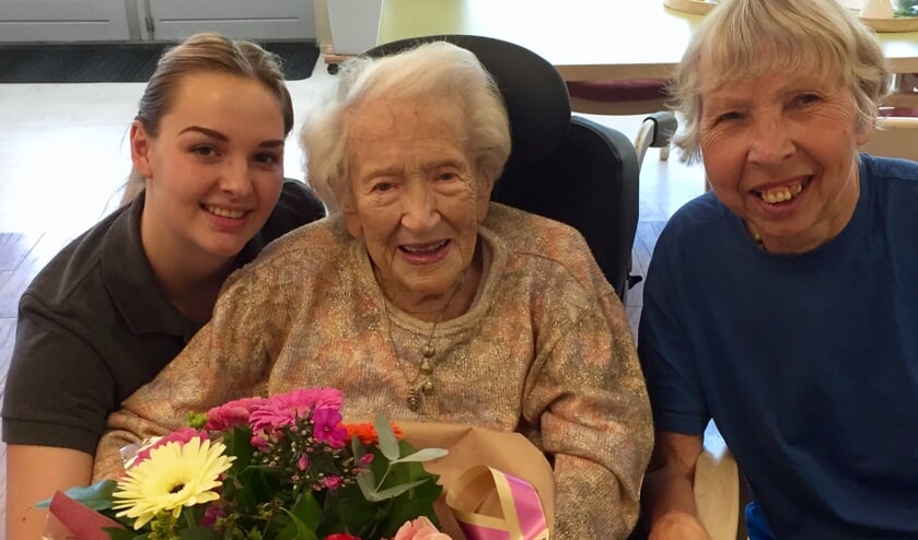 De jarige mevrouw Van Oosterhout is in De Nieuwe Haven in de bloemen gezet. Links stagiaire Amber Kok, rechts bewoonster Marianne Bakker.