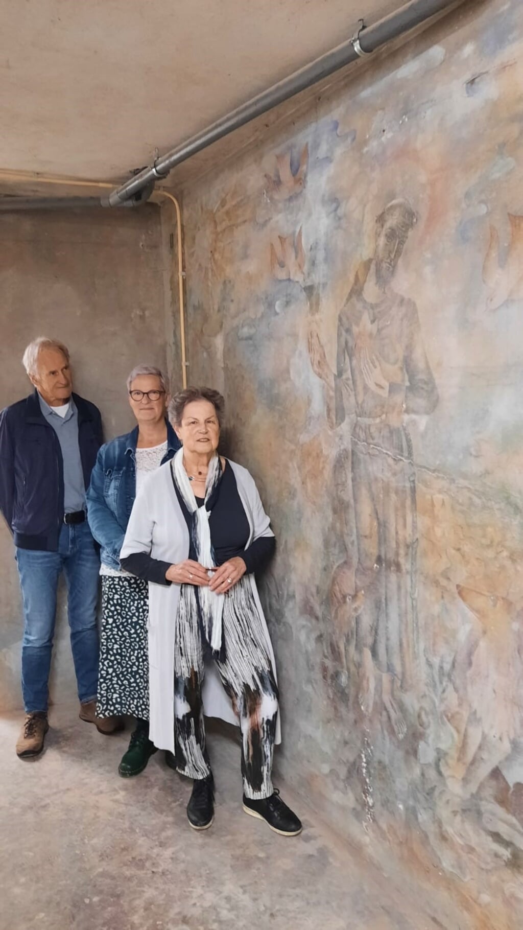 Mevrouw Verhaart-Buijs, haar dochter Kitty en de heer In 't Veld van het Platform Kunst en Cultuur bij de muurschildering in de kelder.
