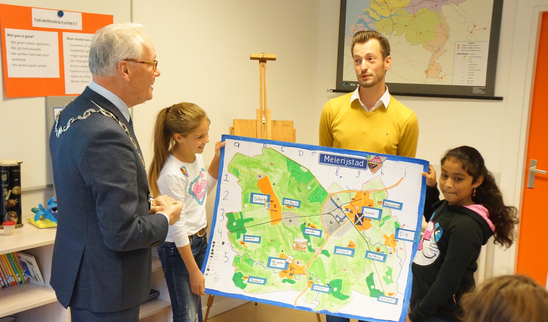 Roos (l) en Sona geven onder toeziend oog van meester Rolf de kaart aan de burgemeester.