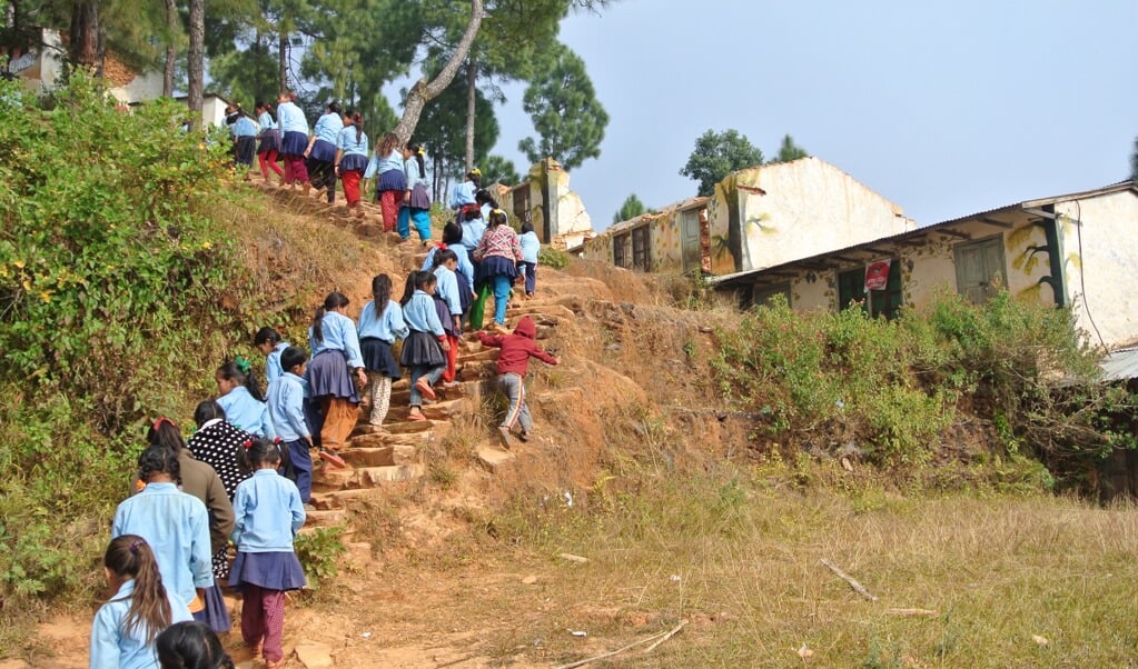 De leerlingen op weg naar hun noodlokalen met op de achtergrond hun door de aardbeving verwoeste school