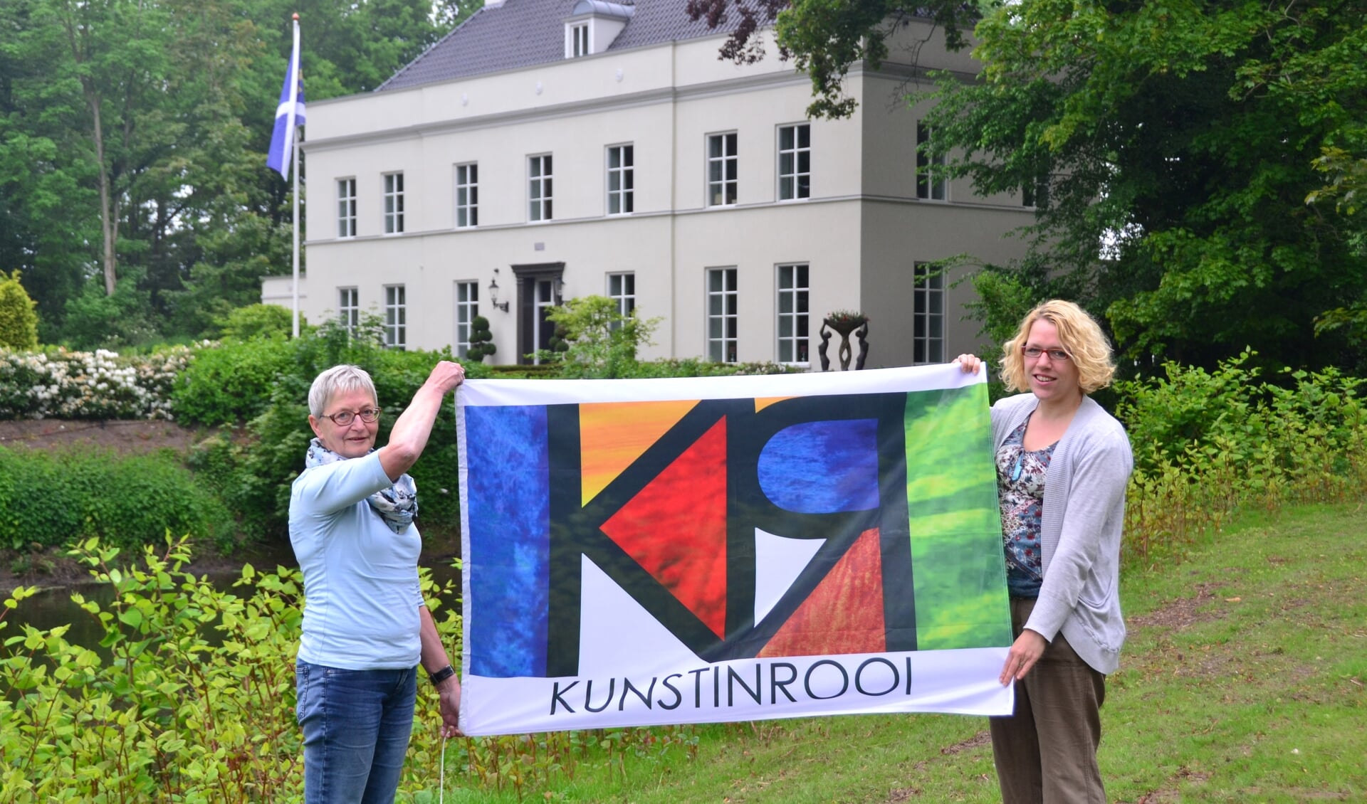 Lia Bekkers en Petra Thoen (r) presenteren de vlag van KUNSTINROOI voor 'De Kolk', één van de deelnemende locaties op 30 en 31 mei