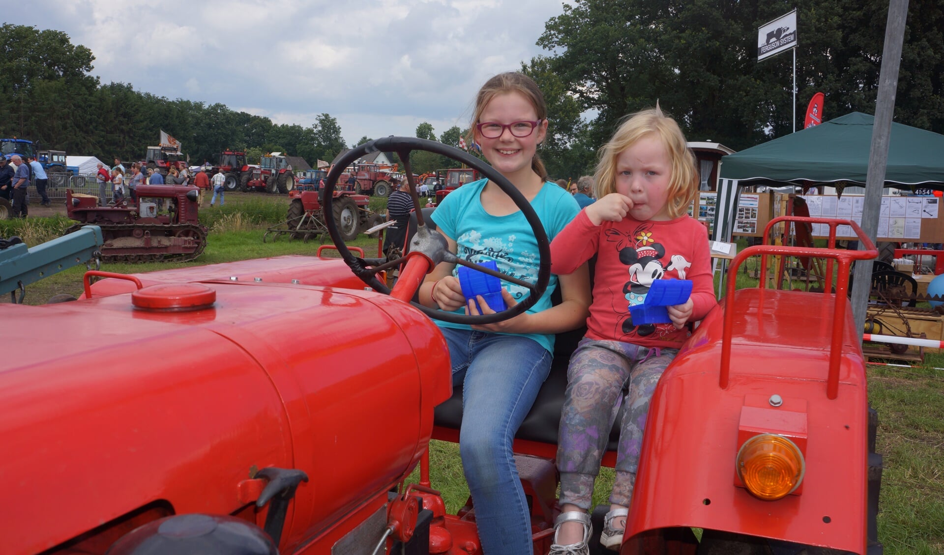 Deze twee meiden rusten even uit op een rode tractor.